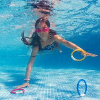 Female Coach In Water Giving Group Of Children Swimming Lesson In Indoor Pool